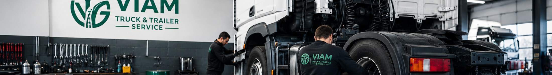 Twee monteurs aan een opgehesen trekker in de werkplaats, met het logo van Viam Truck & Trailer Service op de wand